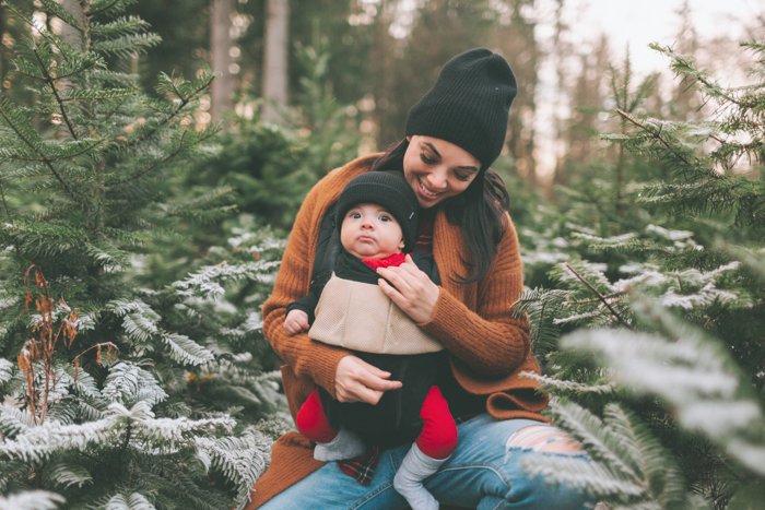 Sweet Christmas photo of a woman holding her baby in front of an outdoor Christmas tree