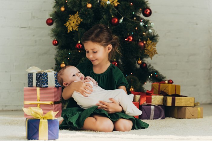 A little girl holding a newborn baby for their first christmas photo shoot