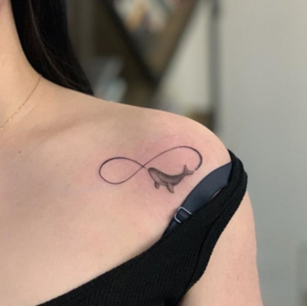 infinity symbol with a flying whale under collarbone tattoo