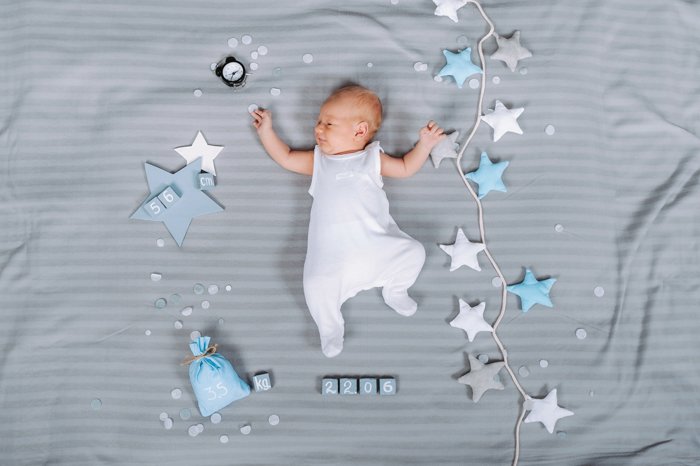Overhead newborn photo idea of the baby resting on a bed beside props and toys